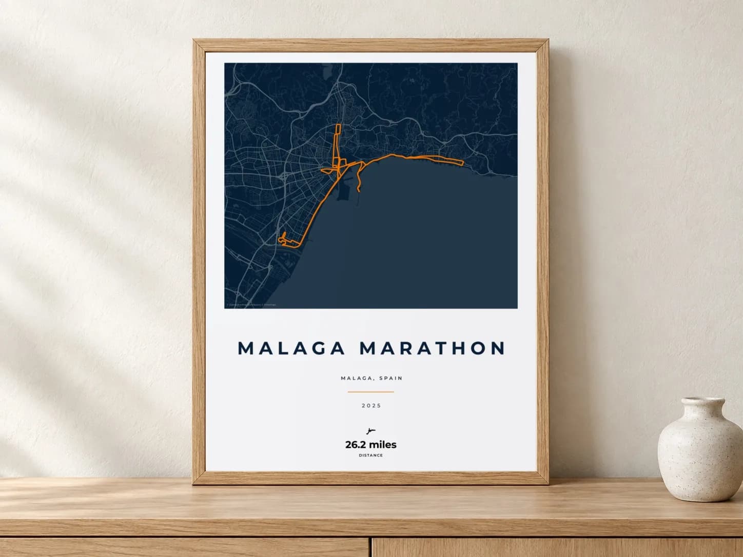 Malaga Marathon 2025 Race Blueprint route print in a light oak frame on a console