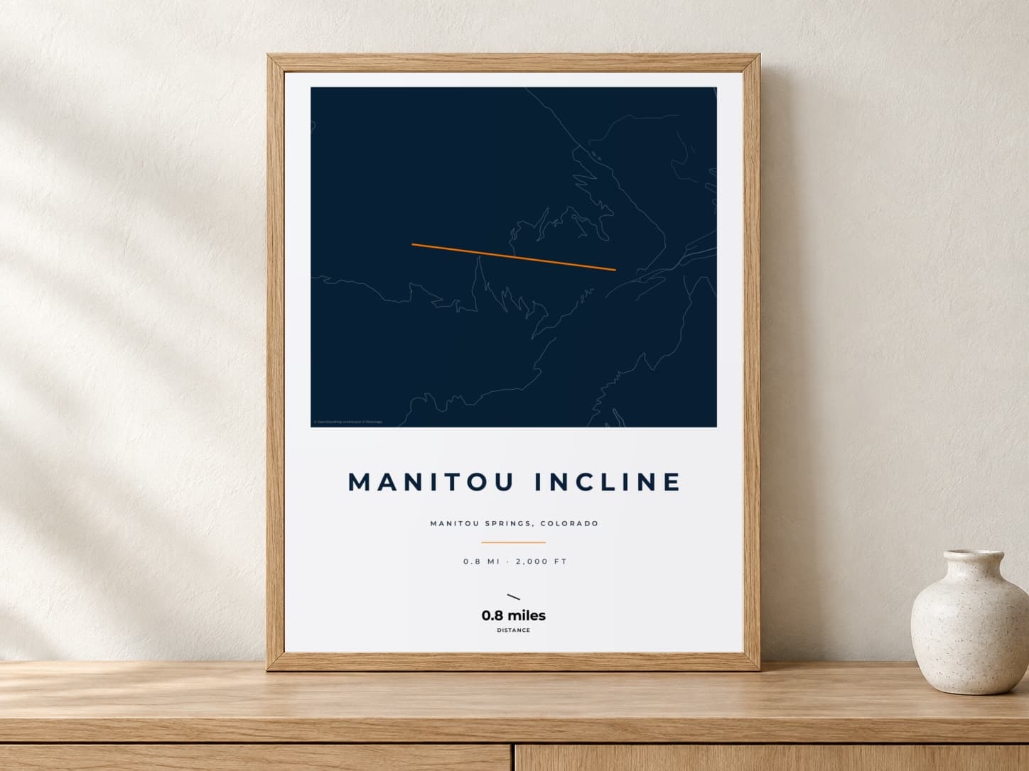 Manitou Incline Race Blueprint route print in a light oak frame on a console