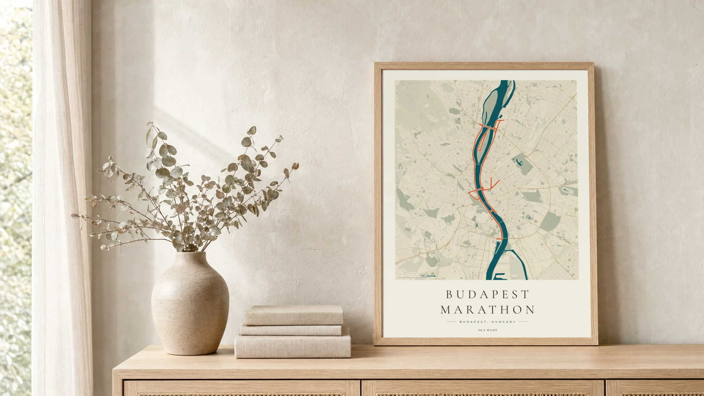 Budapest Marathon 2025 Coastal Atlas route print in a light oak frame on a rattan console