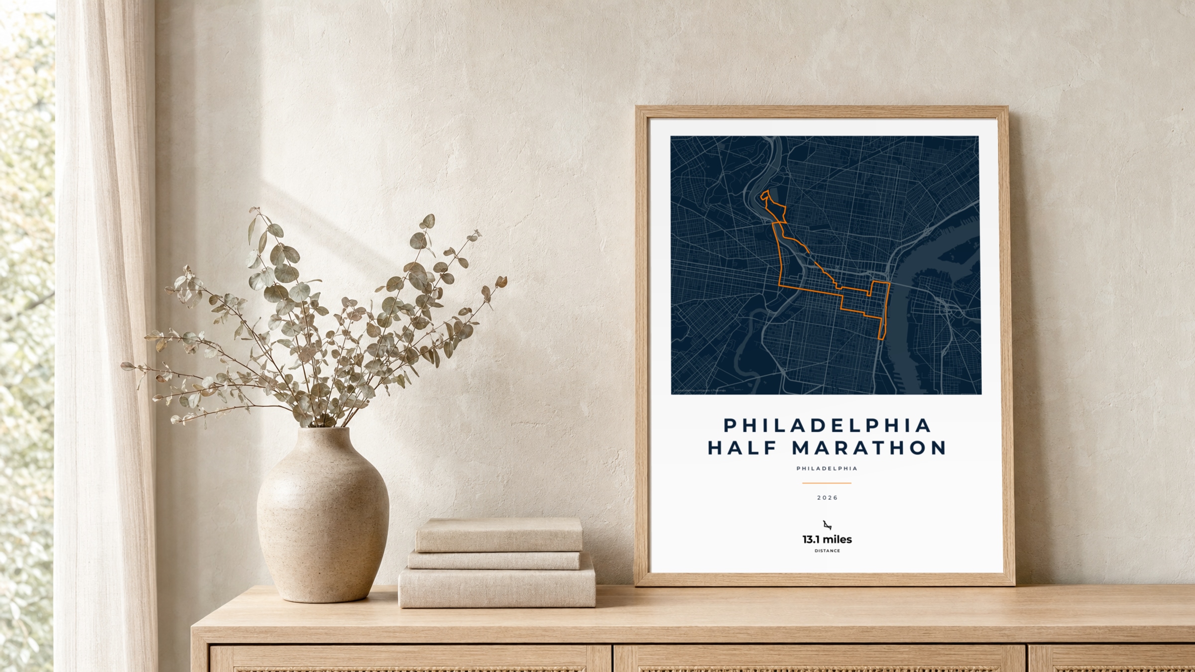 Philadelphia Half Marathon 2026 Race Blueprint route print in a light oak frame on a rattan console