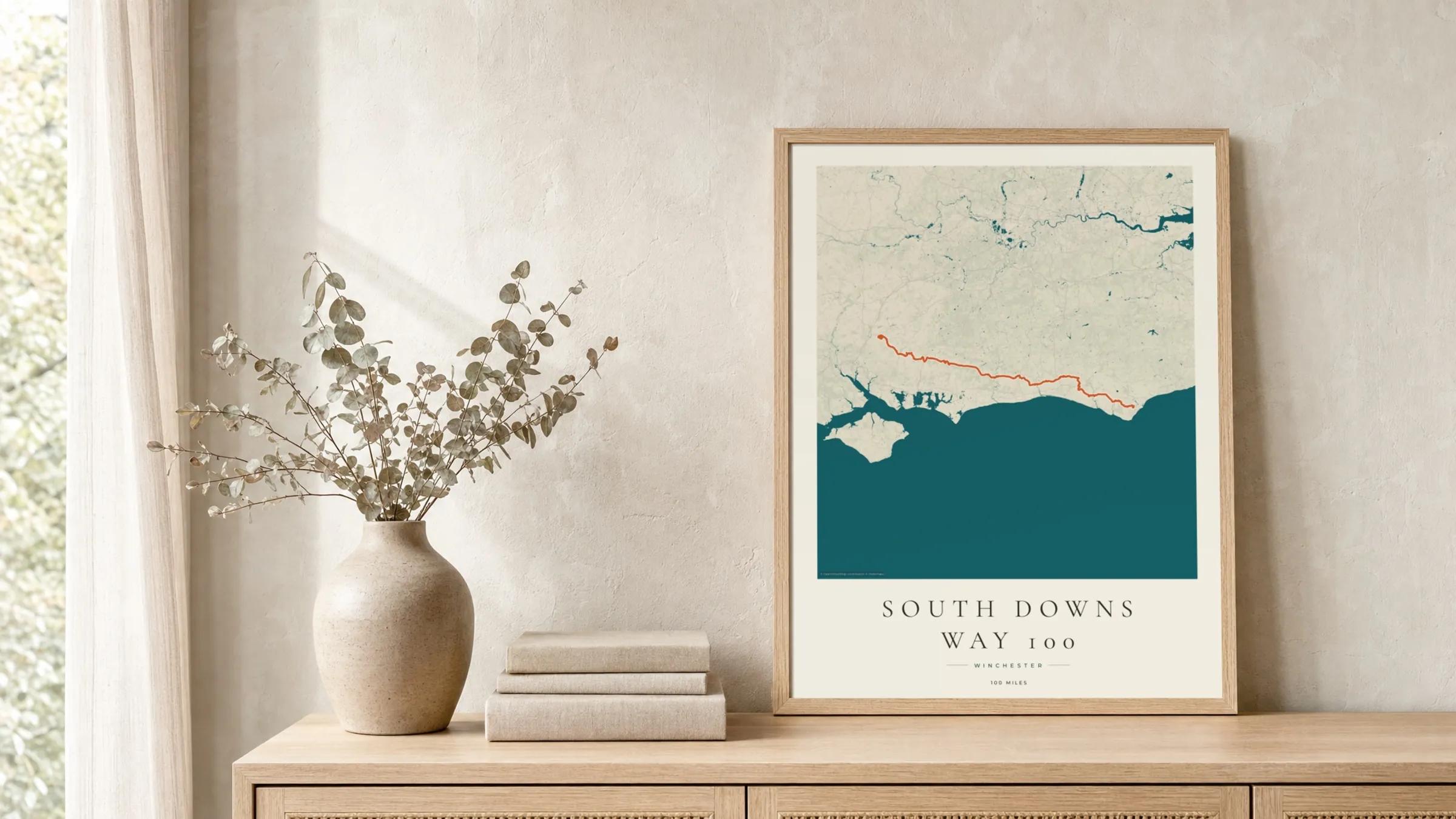 South Downs Way 100 2026 Coastal Atlas route print in a light oak frame on a rattan console