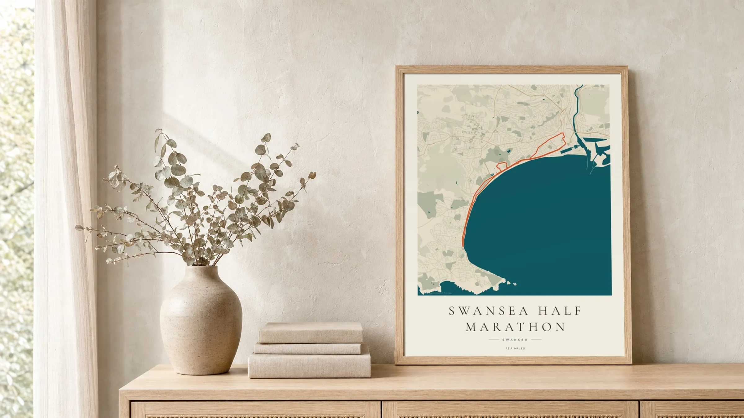 Swansea Half Marathon 2025 Coastal Atlas route print in a light oak frame on a rattan console