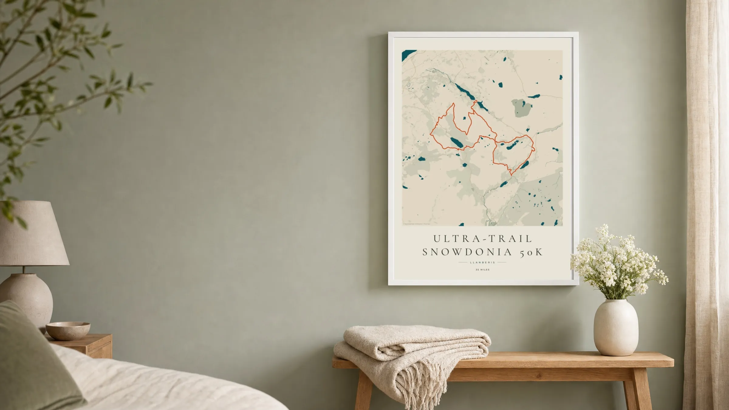Ultra-Trail Snowdonia 50K 2026 Coastal Atlas route print in a white frame on a sage bedroom wall
